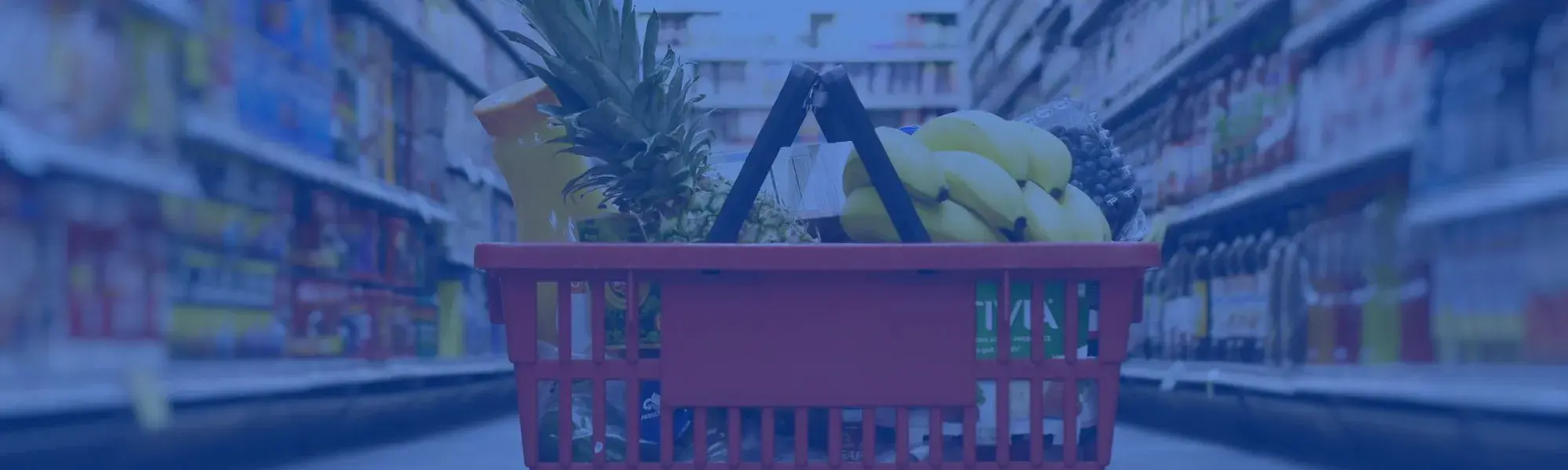 basket full of groceries in center of image; grocery store aisles behind