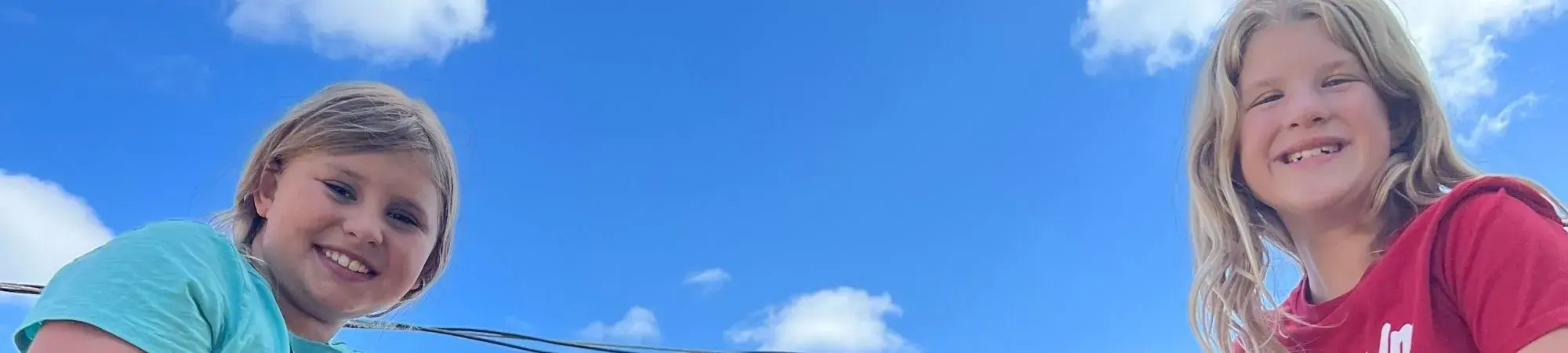 Girls smile in front of blue sky. They are eating Meet Up and Chow Down summer lunches.