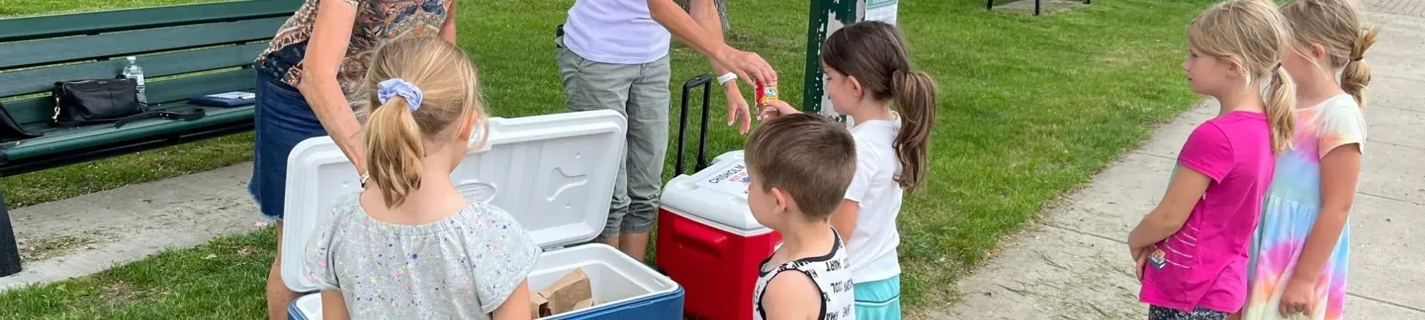 Volunteers hand children free bag lunches from a cooler at the Chisholm Meet Up and Chow Down site