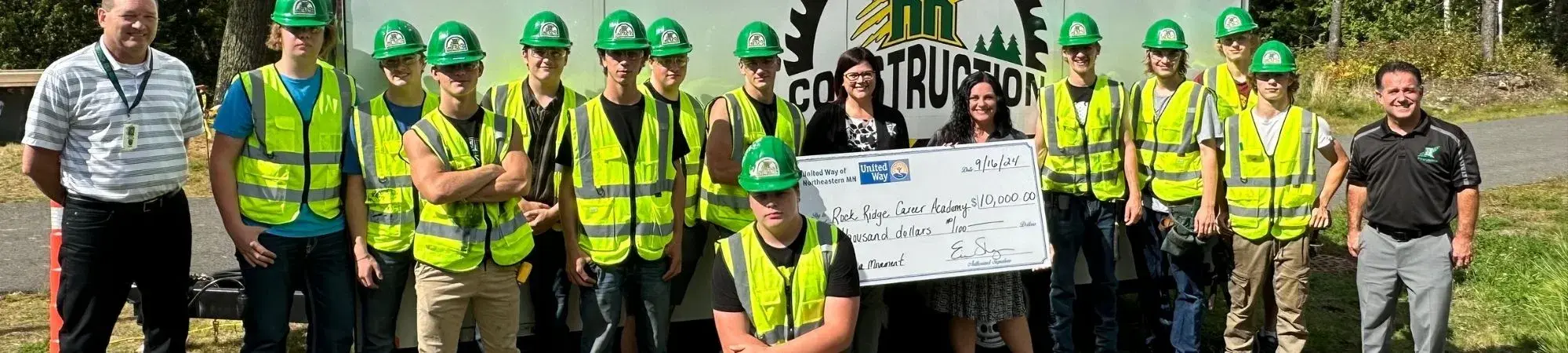 UWNEMN staff presents a check to Rock Ridge High School Career Academy students (all wearing construction gear) to support the career academy